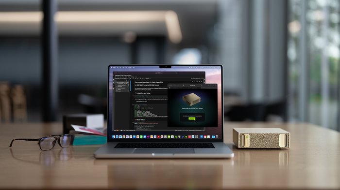 NVIDIA DGX Spark, a small gold-fronted metal box with a fine perforated mesh face, sitting on a wooden desk beside an open laptop that is running the machine's setup screen. The box is roughly the footprint of a paperback.