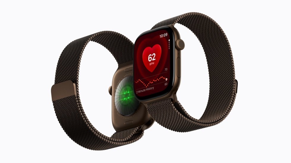 Two Apple Watch Series 12 units in gold with mesh bands, one showing the rear sensor array lit green, the other showing a heart rate reading of 62 BPM with a two-minute history graph.